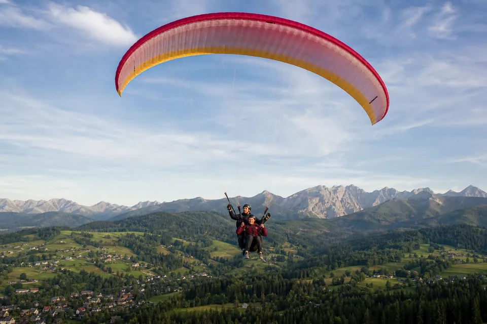Tandem paralotni z pilotem i pasażerem nad zielonymi zboczami Podhala, w tle Tatry